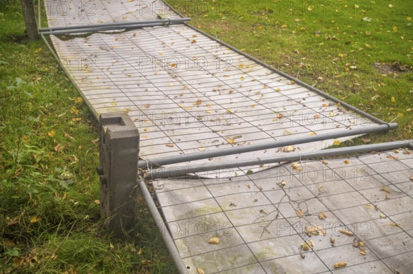 Borken, NRW, Germany, Temporary metal fence panels lying on the ground surrounded by green grass and fallen autumn leaves