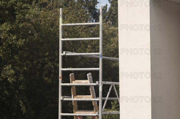 Borken, NRW, Germany, Scaffolding frame with wooden ladder against a building exterior and green trees