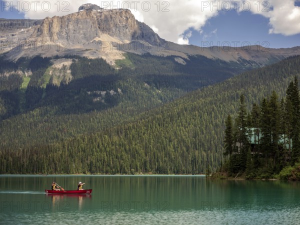 Canoe on Emerald Lake encircled by the Canadian Rocky Mountains and dense forest under a bright sky inside Yoho National Park, British Columbia, Canada, North America