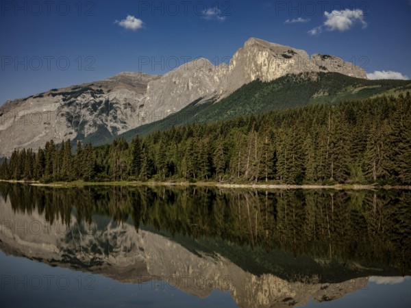 Mountainous landscape of the Canadian Rocky Mountains with dense forest reflected in a calm lake near Canmore, Alberta, Canada, North America