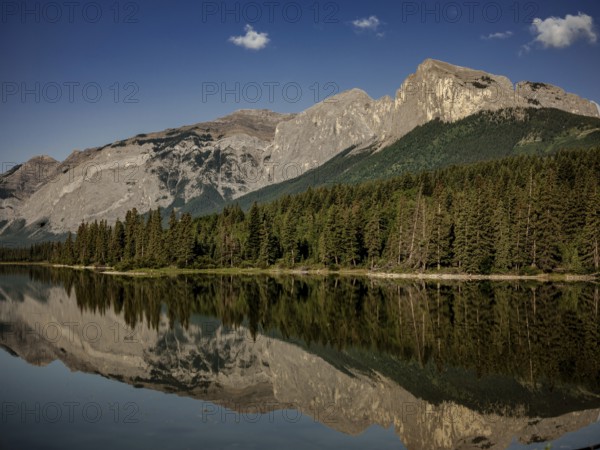 Quiet, reflective waters mirror the surrounding Canadian Rocky Mountains and forest near Canmore, Alberta, Canada, North America