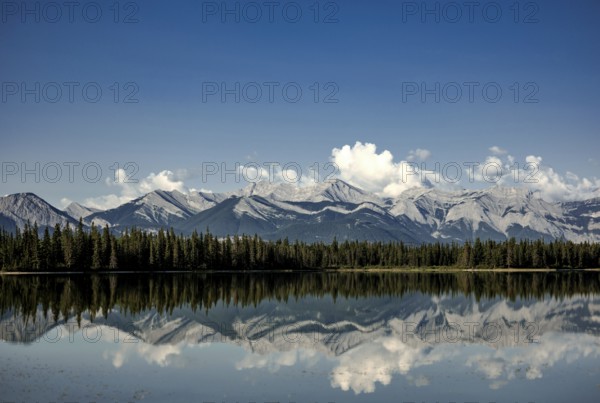 Clear reflections of mountain peaks of the Canadian Rocky Mountains in a lake under fluffy clouds near Canmore, Alberta, Canada, North America