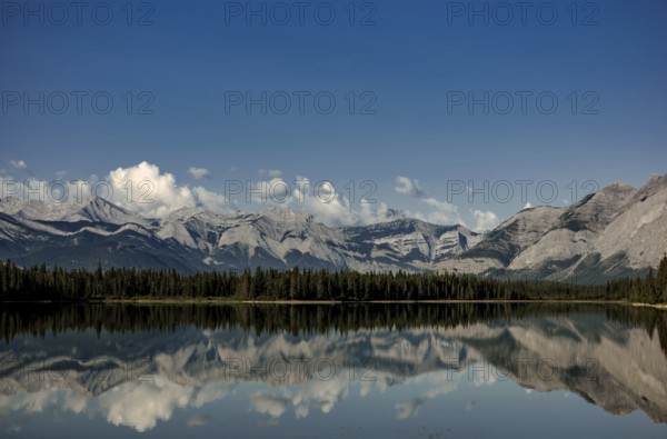 A pristine lake reflecting cloud-capped mountains of the Canadian Rocky Mountains and a peaceful forest near Canmore, Alberta, Canada, North America