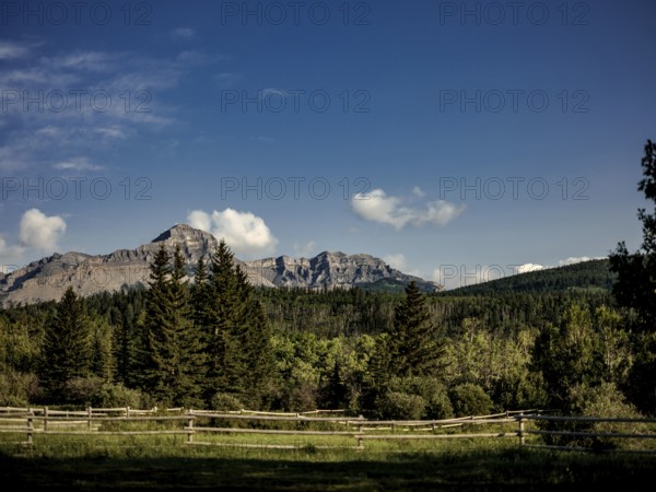 Landscape of mountains of the Canadian Rocky Mountains viewed from a grassy field with a wooden fence near Canmore, Alberta, Canada, North America