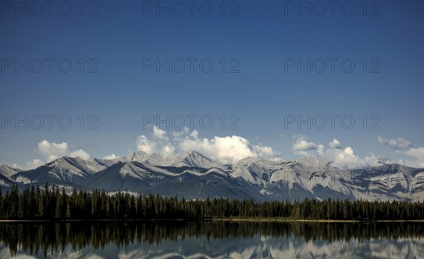 Majestic mountain range of the Canadian Rocky Mountains mirrored in a tranquil lake under a vast blue sky near Canmore, Alberta, Canada, North America