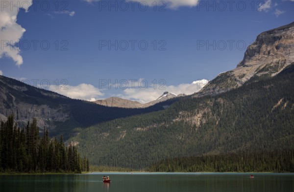 Canoe on a serene Emerald Lake surrounded by the Canadian Rocky Mountains under a blue sky with clouds inside Yoho National Park, British Columbia, Canada, North America