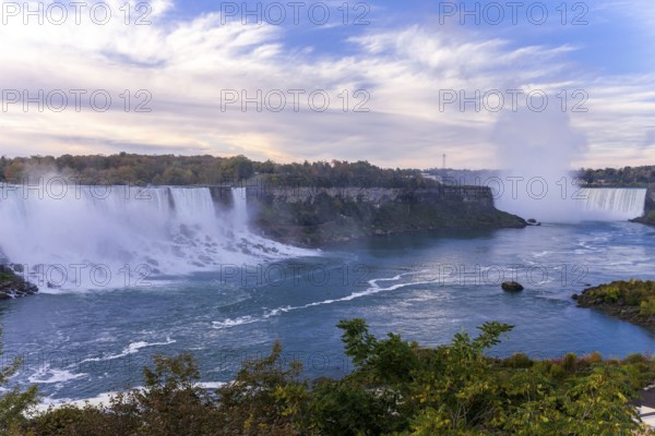 Wide view of the Bridal Veil Falls and the Horseshoe Falls with mist rising under a partly cloudy sky in Niagara Falls, Ontario, Canada, North America