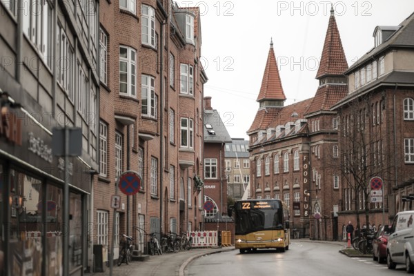A yellow bus navigates a narrow city street lined with red brick buildings on a gray day in Aarhus, Denmark, Northern Europe