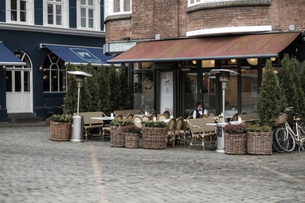 An empty outdoor cafe with wicker chairs and planters on a cobblestone pavement in Aarhus, Denmark, Northern Europe