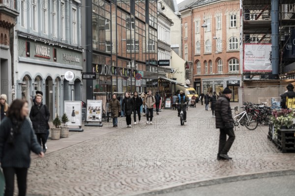 People walk along a bustling cobblestone street lined with various shops in Aarhus, Denmark, Northern Europe