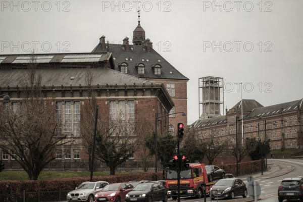 Cars stopped at a red light near historical brick buildings and bare trees on a cloudy day in Aarhus, Denmark, Northern Europe