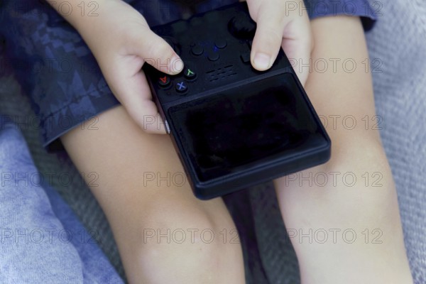 Child's hands holding and playing portable video game console, enjoying entertainment