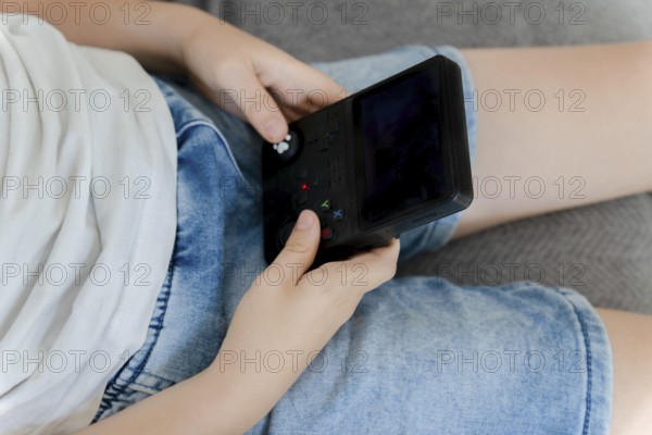 Child hands holding and playing portable video game console during leisure time