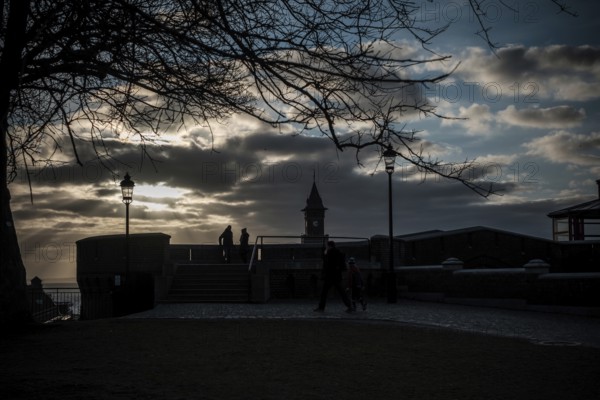 Figures silhouetted against sunset with dramatic clouds, tree, and lampposts in Helsingborg, Sweden, Scandinavia, Northern Europe
