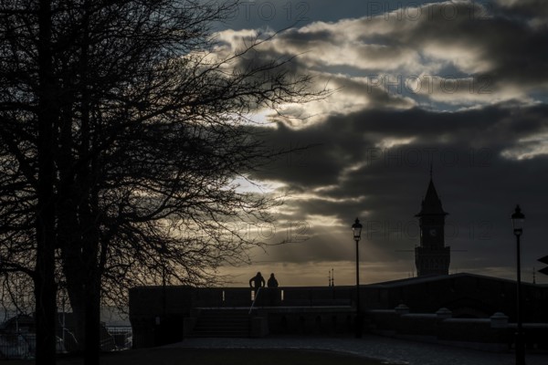 Silhouette scene with tree, lampposts, and tower against a dramatic cloudy sky at sunset in Helsingborg, Sweden, Scandinavia, Northern Europe