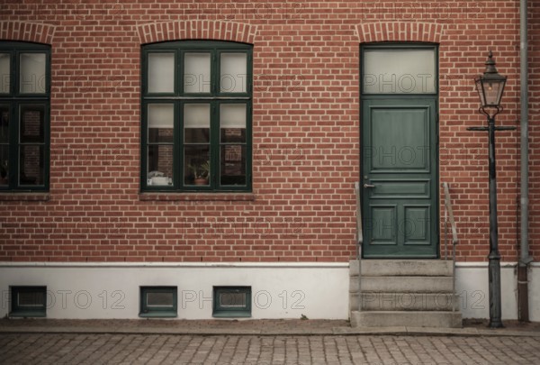 Brick building with a green door and windows, featuring a vintage lamppost on the sidewalk in Helsingborg, Sweden, Scandinavia, Northern Europe