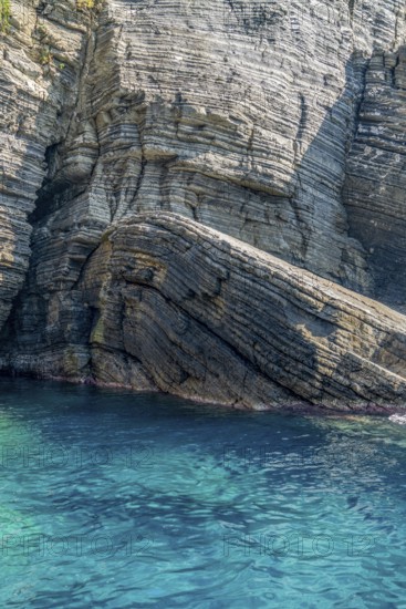 Sunny illuminated detail of the ligurian coast showing a layered rock formation and blue sea