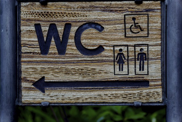 Wooden sign indicating direction of public toilet facilities for all users in ronda, malaga, spain