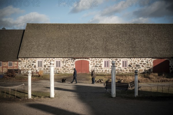 Stone building with red doors on a farm, people walking dogs in foreground in Helsingborg, Sweden, Scandinavia