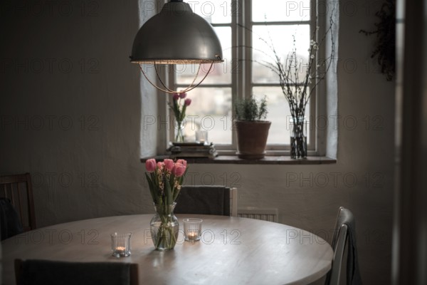 A cozy dining area with a round table, tulips in a vase, and soft lighting from a pendant lamp in Helsingborg, Sweden, Scandinavia