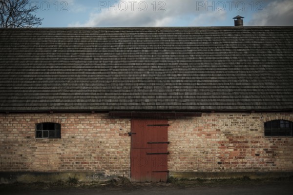 A rustic brick building with a red door under an overcast sky, featuring a chimney in Helsingborg, Sweden, Scandinavia