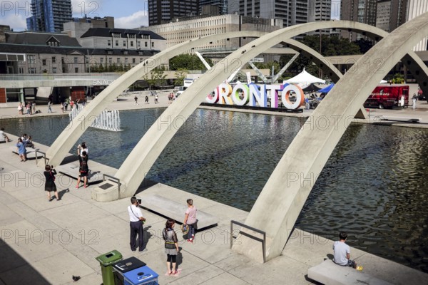 Public plaza in Toronto with arches over a fountain and people enjoying the sunny day in Toronto, Ontario, Canada, North America