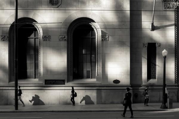 Black and white urban scene with people walking past a sunlit building casting strong shadows in Toronto, Ontario, Canada, North America
