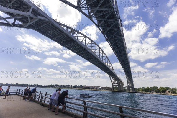 Viewers on a riverside pier looking at the expanse of the Blue Water Bridge connecting Canada and the United States of America, along the St. Clair River leading to Lake Huron in Sarnia, Ontario, Canada, North America
