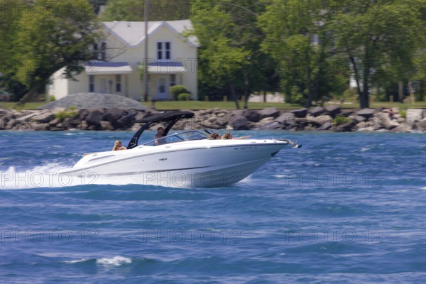 A speedboat glides quickly across the water with trees and houses in the background along the St. Clair River leading to Lake Huron in Sarnia, Ontario, Canada, North America