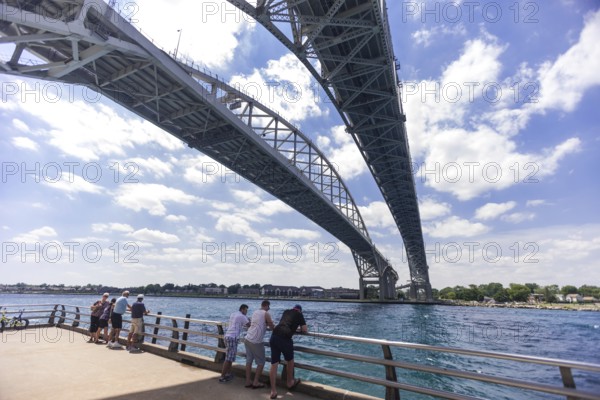 People enjoying the river view underneath the Blue Water Bridge, connecting Canada to the United States of America on a clear day, along the St. Clair River leading to Lake Huron in Sarnia, Ontario, Canada, North America