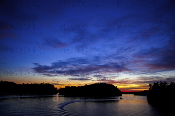 Boat sails on a serene lake during sunset, creating a vivid twilight sky in Muskoka, Ontario, Canada, North America