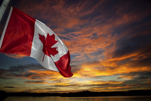 The Canadian flag waves against a vibrant sunset sky filled with colorful clouds in Muskoka, Ontario, Canada, North America