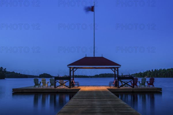 A tranquil lakeside dock with chairs and a flag at dusk in Muskoka, Ontario, Canada, North America