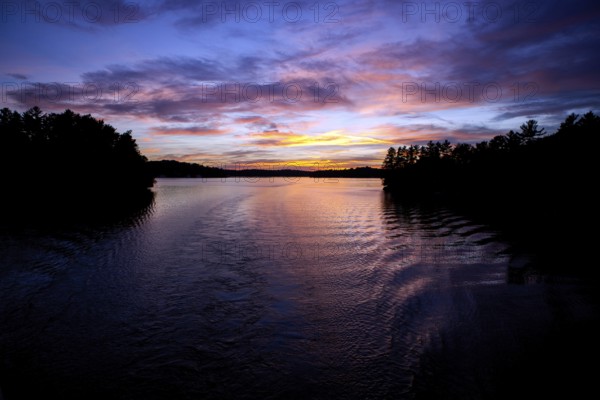 Calm water reflects a colorful evening sky, creating a peaceful twilight landscape in Muskoka, Ontario, Canada, North America