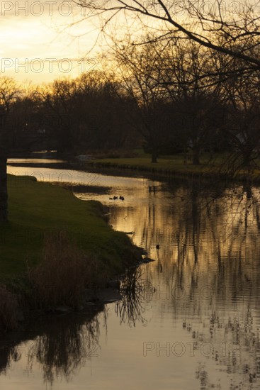 Tranquil scene of a creek at sunset with silhouetted trees and warm reflections in the water in St. Marys, Ontario, Canada, North America