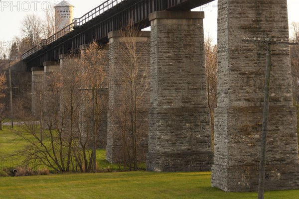 Image of a stone bridge structure with green grass and trees, highlighted by warm tones in St. Marys, Ontario, Canada, North America
