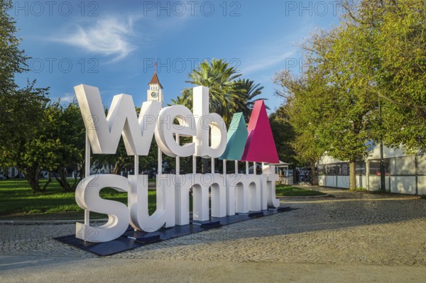 Nov 6, 2024 - Lisbon, Portugal: Big Web Summit sign displayed outdoors in park with lush palm trees on sunny day clear blue skies. Major technology conference, internet technology, emerging technology, marketing, AI solution, spirit of innovation