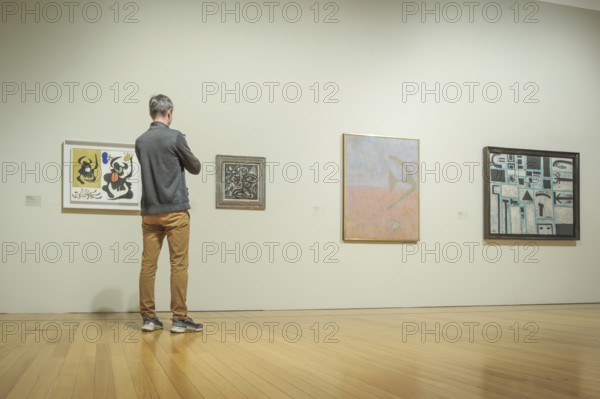 Jan 13, 2024 - Lisbon, Portugal: visitor in gray jacket and tan pants observe abstract artworks displayed on white walls of Berardo Collection Museum, deeply engaged in contemplation in artistic details. Wooden floor, serene atmosphere, minimalistic