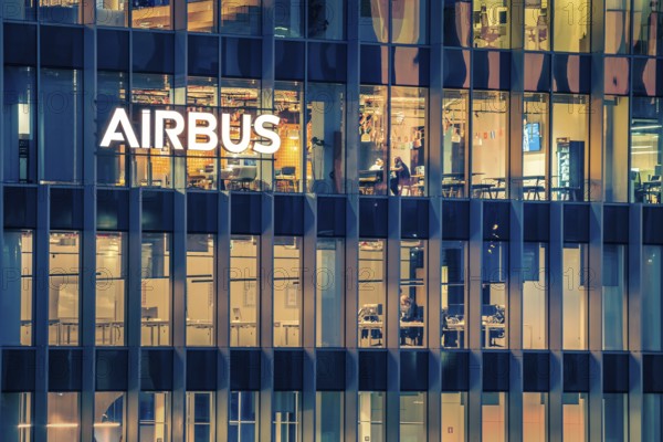 Jan 15, 2025 - Lisbon, Portugal: Night view of the Airbus office building or headquaters with bright illuminated logo and modern glass facade. Interior of workspace with people at desks, leading aerospace company, modern architecture, daily corporate