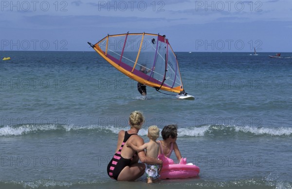 Family at the beach watching windsurfing. Two children with an adult, enjoying the sunny day