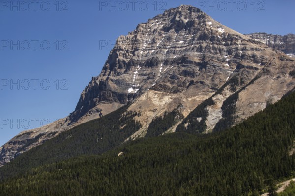 Dramatic mountain peak rising above a dense green forest as viewed from the Trans Canada Highway in British Columbia, Canada, North America