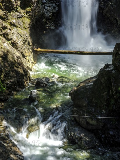 Cascading waterfall over rocks in sunlight in forest inside Cascade Falls Regional Park, Deroche, British Columbia, Canada, North America