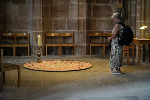 Woman standing in front of lit candles in a church as an expression of devotion, St Lorenz Church, Nuremberg, Middle Franconia, Franconia, Bavaria, Germany