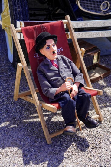 Oldtimer Classic, Gala International Concours d'Elegance Schwetzingen 2025, Germany, Europe, Charlie Chaplin doll sits relaxed in a deckchair at an exhibition of classic cars
