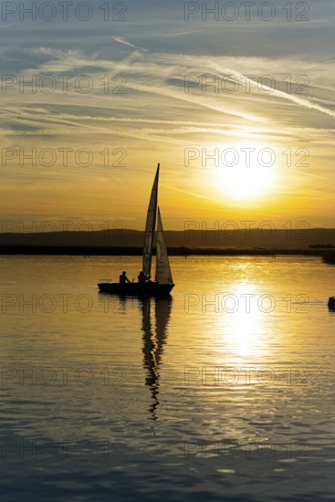Lake Neusiedl, Burgenland, Austria, Europe, Sailboat gliding on calm water in the golden glow of the setting sun, Sailboats on Lake Neusiedl