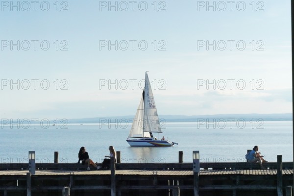 Lake Neusiedl, Burgenland, Austria, Europe, A sailboat sails calmly on a lake while people relax on the jetty, Sailboats on Lake Neusiedl