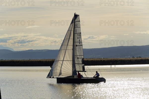 Lake Neusiedl, Burgenland, Austria, Europe, Two people sailing in a boat in the calm evening mood with mountains in the background, Sailing boats on Lake Neusiedl