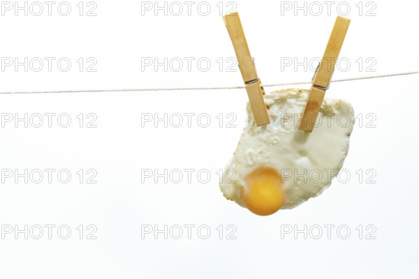 Clothespins holding fried egg on clothesline against white background, creating a quirky and unusual image