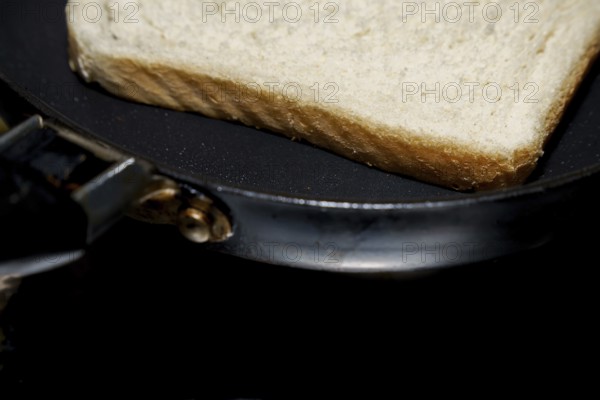 Close-up of a single slice of white bread toasting in a frying pan, suggesting a simple breakfast preparation