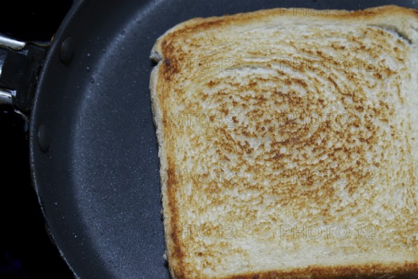 Close-up of a single slice of toasted white bread in a frying pan, showing the texture and golden-brown color